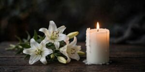 A lit white candle beside white lilies for sympathy blessings